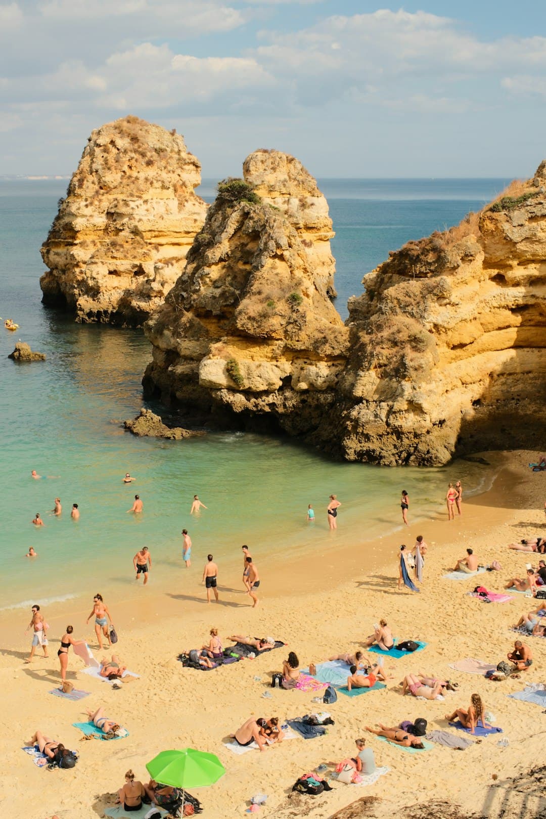People relax on a sandy beach near rock formations