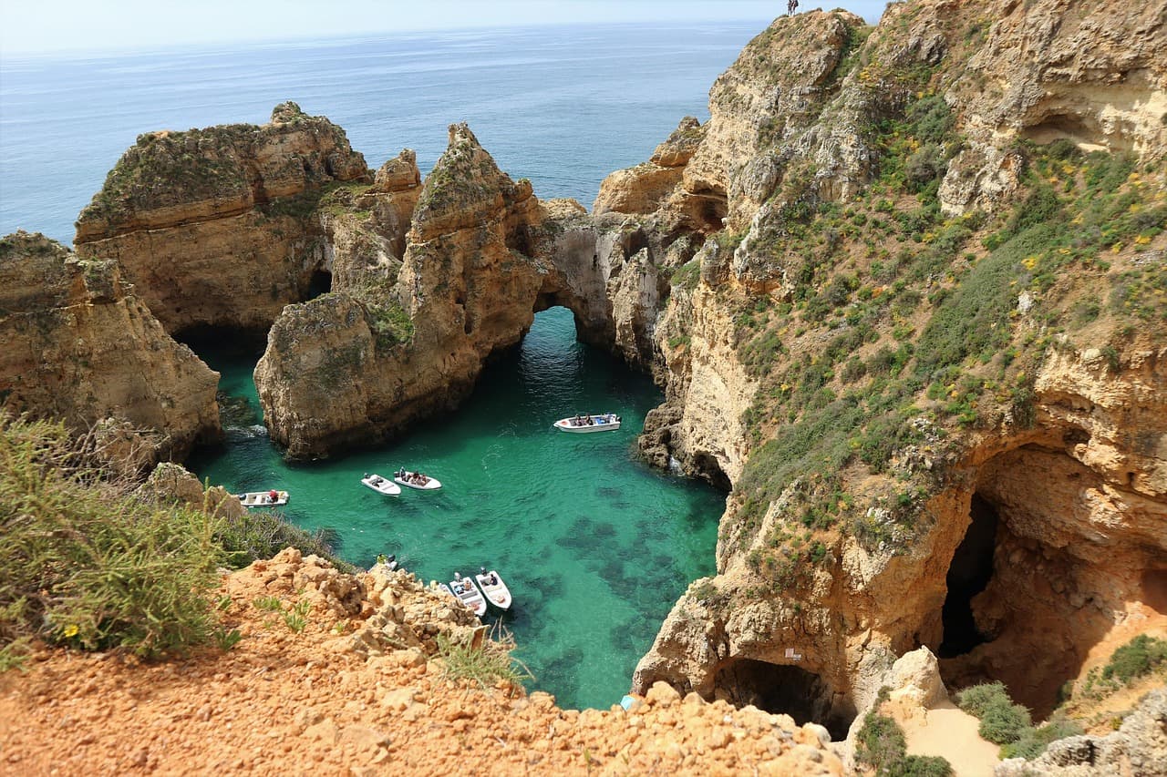 Scenic view of coastal rock formations and turquoise waters with small tour boats in the Algarve, Portugal.
