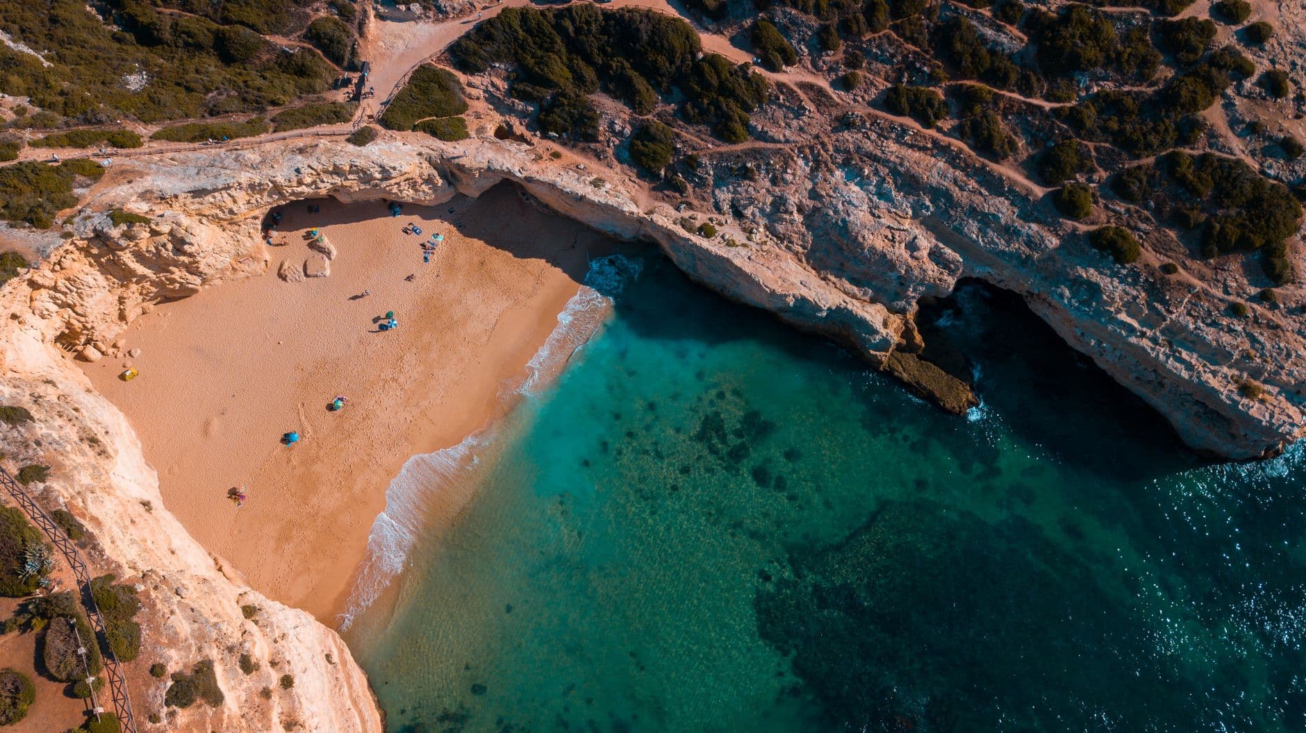 Aerial view of a secluded hidden beach surrounded by dramatic golden cliffs and clear turquoise water in Algarve, Portugal