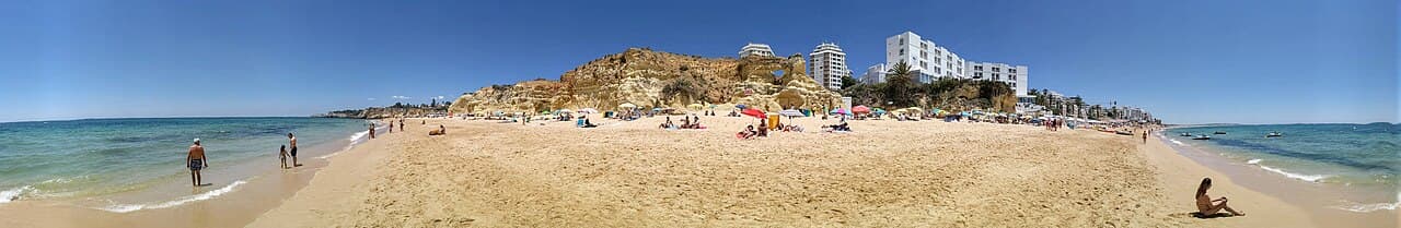 Panoramic view of Praia de Armação de Pêra from the surf, showing the Holiday Inn, cliffs, and more